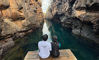 Couple sitting at the edge of las grietas in Galápagos.